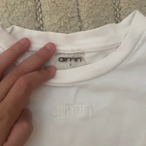 Vit t-shirt från Aim'n i bomull - Säljer en clean vit t-shirt från Aim'n i storlek S. T-shirten har klassisk rund hals och korta ärmar, med diskret Aim'n-logga broderad framtill. Perfekt basic att ha i garderoben, kan användas till träning också. (Knappast använd)