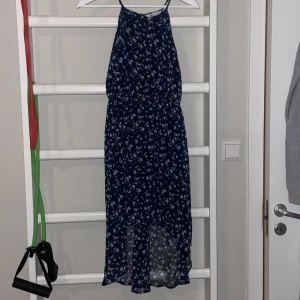 Mörkblå blommig långklänning från Ellos - Säljer en mörkblå långklänning från Ellos med vita blommor. Klänningen har smala axelband, elastisk midja och ärmlös design. Materialet är lätt och luftigt, perfekt för varma dagar. Använd 2 ggr 