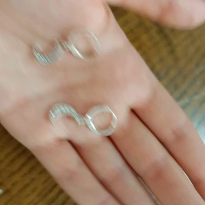 Silvriga örhängen med glittriga detaljer - Säljer ett par snygga silvriga örhängen med glittriga stenar. De har en unik form med en rund del och en böjd, stensatt del som ger extra bling. Perfekt för dig som gillar att sticka ut med dina accessoarer.