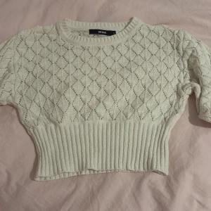 Vit stickad croppad tröja BikBok - Superfin vit stickad tröja från BikBok i croppad modell. Tröjan har ett snyggt hålmönster i diamantform och bred ribbad nederkant. 