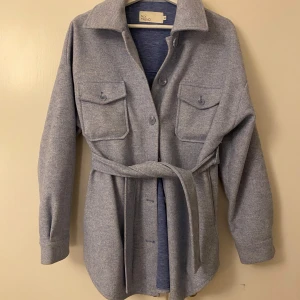 Ljusblå jacka från NLY Trend - Säljer en ljusblå jacka från NLY Trend i storlek 32. Jackan har knappar framtill, två stora bröstfickor med lock och ett bälte i midjan. Den är långärmad och har en avslappnad, oversized passform. Perfekt att slänga över en crop top för en chill look. Nypris 749kr och helt slutsåld på hemsidan. Nästan helt oanvänd💕priset kan diskuteras. Stor i storleken 