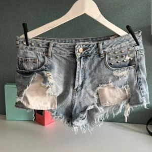 Ljusa jeansshorts med nitar och slitningar - Snygga ljusblå jeansshorts med råa, fransiga kanter och stora slitningar framtill. De är i storlek 40 men passar även om du har storlek 38🥰