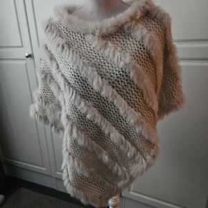 Soyaconcept beige poncho äkta päls - Oanvänd Elegant poncho från Soyaconcept. Denna poncho har en unik design med detaljer i kaninpäls som ger en lyxig känsla. Perfekt för att lägga till ett stilfullt lager till din outfit.