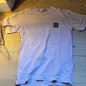 Ljusrosa  t-shirt - Snygg ljusrosa t-shirt  med klassisk rund hals och korta ärmar. På bröstet sitter den ikoniska Stone Island-patchen i svart. T-shirten är gjord i mjuk bomull och har en clean, normal passform som funkar till streetwear-stilen.