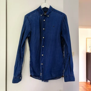 Blå skjorta från Morris - Snygg blå skjorta från Morris med klassisk krage och vita knappar. Skjortan har lång ärm och en liten broderad logga på bröstet. 