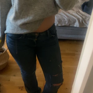 Mörkblå/blå slitna jeans bootcut/flare - Säljer ett par mörkblå/blå jeans med snygga slitningar på benen. Jeansen har  låg midja och är bootcut/flare.Materialet är jeans i bomull med lite stretch.