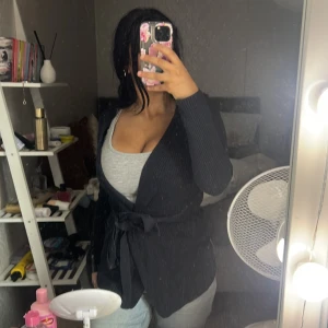 Svart stickad cardigan jacka med bälte - Mysig svart stickad cardigan jacka med knytbälte i midjan. Långärmad och med en snygg, enkel design som passar perfekt till jeans eller leggings. Jackan har en loose fit och är superenkel att slänga på sig när det är lite kyligt ute.