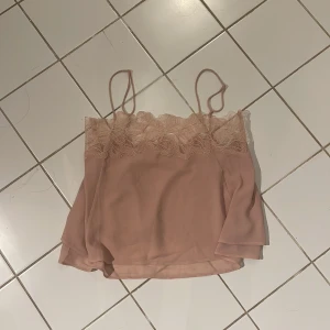 Ljusrosa spetslinne från H&M Edition - Supersött ljusrosa linne från H&M Edition i storlek XS. Toppen har tunna axelband och vacker spetsdetalj längs överdelen. Materialet är lätt och skönt. Använd 1 gång