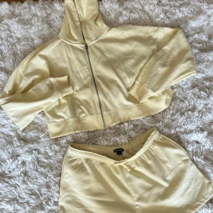 Ljusgult mjukisset från Boohoo DSGN Studio - Snyggt ljusgult set med shorts från Boohoo DSGN Studio med broderad logga framtill. De har elastisk midja med snörning och är gjorda i mjuk bomull, perfekta för chill dagar eller träning. Passformen är normal och de är riktigt sköna att ha på sig. Nyligen inköpta men aldrig använda endast testat på. 