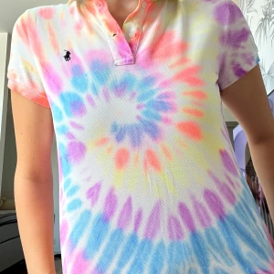 Färgglad tie-dye piké från Ralph Lauren - Säljer en superfin pikétröja från Ralph Lauren med färgglatt tie-dye mönster i rosa, blått, lila, gult och orange. Klassisk krage, korta ärmar och knappar framtill. Ikoniska broderade loggan på bröstet. Perfekt för dig som gillar färg och vill sticka ut!     STORLEK- XL 16 år - men går att användas i fall man har S i vuxen storlek (har själv det)