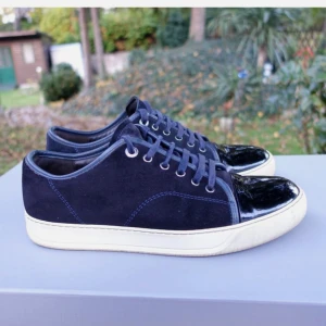 Mörkblå lanvin sneakers med lackad tå - Snygga mörkblå sneakers med snörning och vit platt sula. Skorna har en unik detalj med lackad svart tå som ger extra edge. Ovandelen är i mocka och de passar perfekt för dig som gillar stilrena men ändå coola skor.