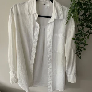 Vit overssize skjorta - Stilren vit skjorta från H&M med klassisk krage och knappar framtill. Skjortan har lång ärm och bröstficka, tillverkad i mjuk bomull. Den är overssize så man kan gå ner en eller två storlekar och passar lika bra ändå. 