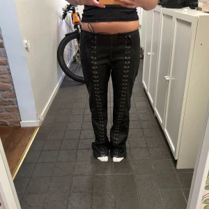 Svarta läderbyxor med snörning - Svarta skinnbyxor från Pull&Bear med cool snörningsdetalj längs hela framsidan av benen. Byxorna har rak passform och midwaist, vilket ger en snygg och modern look. Perfekta för dig som vill sticka ut med en edgy stil.
