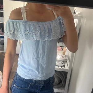 Ljusblå offshoulder topp från H&M - Superfin ljusblå offshoulder topp från H&M med bred volangkant och broderade blommor längs axlarna. Smockad nederkant för skön passform. Perfekt till jeans eller kjol när du vill ha en söt och somrig look. priset går att diskuteras