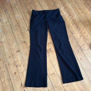 Svarta bootcut kostymbyxor från Nelly - Svarta kostymbyxor från Nelly i bootcut-modell med klassisk passform. Byxorna har hällor för bälte och stängs med knapp och dragkedja. Perfekta för en clean och stilren look.