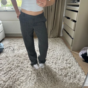 Grå kostymbyxor från Zara - Snygga grå kostymbyxor från Zara med klassisk rak passform och bälteshällor. Byxorna har diskreta fickor och stängs med dragkedja och knapp. Perfekta för en clean och stilren look. Materialet är mjukt och känns bekvämt hela dagen.