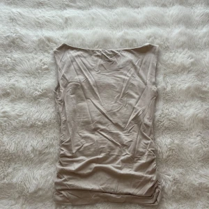 Beige topp - Supersnygg beige topp i mjukt material med ”scrunch” detaljer på sidorna. Ärmlös och figurnära passform som framhäver siluetten. Från Gina Tricot ”Soft touch”