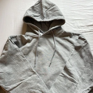 Grå hoodie med huva och snörning - En stilren grå hoodie med klassisk huva och snörning. Tröjan är i mjuk bomullsmix och har en relaxed passform. Perfekt för chill dagar eller när du vill ha en enkel och clean look. Långärmad och utan tryck eller mönster.