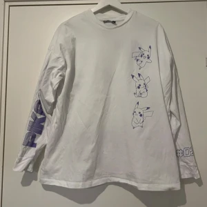 Vit Pikachu långärmad tröja Pokémon - Vit långärmad tröja från ASOS x Pokémon med stora lila Pikachu-prints fram, bak och på ena ärmen. Coolt tryck med #025 Pikachu och Pokémon-logga. Perfekt för dig som älskar anime och gaming. Tillverkad i mjuk bomull, relaxed fit och crewneck.