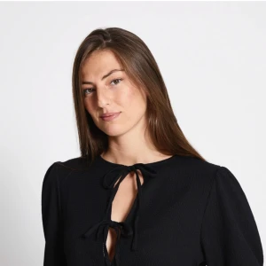 Svart blus med knyt från Lager 157 - Supersöt svart blus från Lager 157 med två knyt framtill och lätt puffade korta ärmar. Blusen har en luftig passform och volang nedtill som ger en chill vibe. Perfekt att matcha med jeans eller kjol för en cool look.