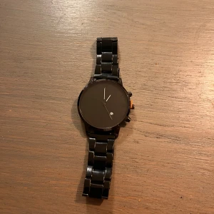 Svart stilren klocka med länkarmband - Snygg svart klocka med minimalistisk design och rund urtavla. Klockan har ett svart metallänkarmband och diskreta visare. Perfekt för dig som gillar en clean och modern look. Liten datumvisning på urtavlan och detaljer i svart ger en cool känsla.