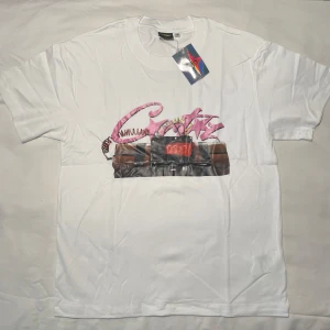 Corteiz T-shirt dynamit  - Vit t-shirt från Notime4luv i bomull med coolt tryck framtill och stor svart text 'NOTIME4LUV' på ryggen. Framsidan har ett färgstarkt grafiskt motiv med rosa och bruna detaljer. Klassisk rund hals och korta ärmar. Perfekt för dig som gillar statement-plagg.