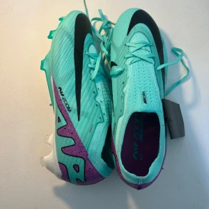Nike Mercurial Air Zoom fotbollsskor - Nike Mercurial Air Zoom fotbollsskor i turkos med svarta detaljer och lila inslag på hälen. Skorna har snörning, platt sula med dobbar och är tillverkade i syntetmaterial för bästa grepp och känsla på planen. Perfekta för dig som vill sticka ut på matchen. 10/10 knappt använd. Priset kan diskuteras vid snabb affär.