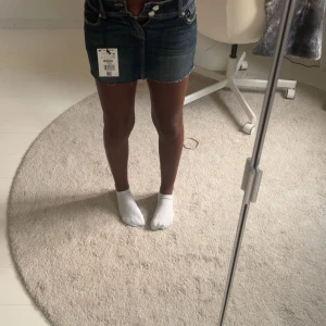 Mörkblå jeanskjol med rå kant - Snygg mörkblå jeanskjol med rå, fransig kant nertill och klassiska fickor fram och bak. Kjolen har bälteshällor och stängs med knapp och dragkedja. 