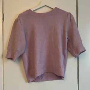 Ljuslila stickad tröja med puffärm - Superfin ljuslila stickad tröja med korta puffärmar och breda ribbade muddar vid ärmslut och nederkant. Tröjan har en rund halsringning och är lite loose i passformen, perfekt för dig som gillar en chill och söt stil.