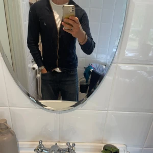 Mörkblå kofta från Peak Performance - Snygg mörkblå kofta från Peak Performance i kashmirblandning. Brun kant längs knäppningen och bruna mockadetaljer på armbågarna. Klassisk v-ringning och knappar framtill. Perfekt för dig som gillar stilrena och bekväma plagg. Helheten är bra men säljs billigt då det finns noppror