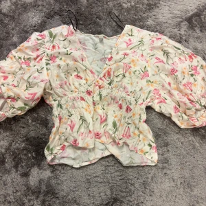 Blommig omlottblus med puffärmar - Supersöt blommig omlottblus med v-ringning och puffiga ärmar. Blusen har smockad midja och volangig nederkant. Använd kanske 5-10 gånger storlek L men passar även M 