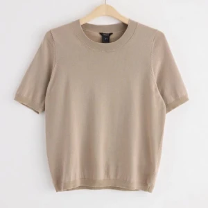 Beige stickad kortärmad tröja!  - En stilren beige stickad tröja från Lindex i storlek M. Tröjan har korta ärmar, rund halsringning och ribbade kanter vid ärmslut och nederkant. Tröjan är endast använd 1-2 gånger. (Porto tillkommer) 