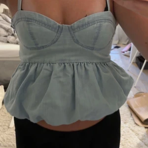 Ljusblå peplum korsett-topp - Supersöt ljusblå korsett-topp med peplumvolang och smala axelband. Toppen har markerade kupor och en figurnära passform upptill som ger en snygg siluett. Perfekt att styla med både jeans och kjol för en trendig look.