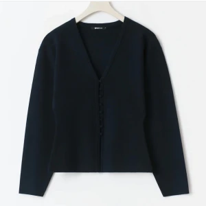 Svart kofta med v-ringning från Gina Tricot - Stilren från Gina Tricot i marinblått med v-ringad hals och snygga knappar framtill. Långärmad och i mjukt material som sitter skönt på kroppen. Perfekt att slänga över ett linne eller bära som den är för en clean look. Endast använd 2 ggr.