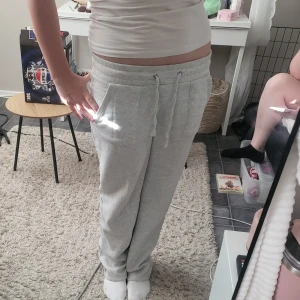 Grå mjukisbyxor med snörning - Säljer ett par ljusgrå mjukisbyxor med snörning i midjan och stora fickor framtill. Byxorna har en relaxed passform och är gjorda i mjukt bomullsmaterial, perfekta för chill dagar hemma eller när du vill vara extra bekväm.