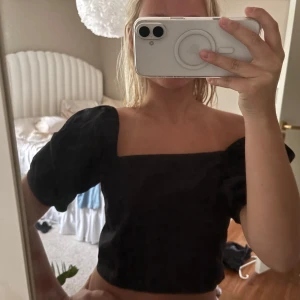 Svart croppad blus med puffärm - Säljer en svart croppad blus med fyrkantig urringning och puffiga korta ärmar. Ärmarna har broderade detaljer som ger en extra touch. Perfekt för dig som gillar trendiga och stilrena plagg med lite edge.