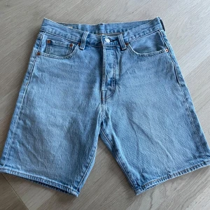 Levi's ljusblå jeansshorts W29 - Ljusblå jeansshorts från Levi's med klassisk femficksdesign, knappgylf och brunt läderpatch bak. Modellen är rak och lite längre i benen, perfekt för en chill sommarstil. Snygga kontrastsömmar och slitstarkt denimtyg.