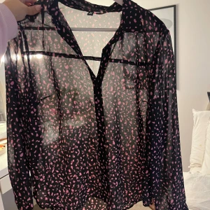 Skjorta - Säljer en svart transparent skjorta från H&M med rosa prickigt mönster. Skjortan har lång ärm, klassisk krage och knappar framtill. Perfekt för dig som gillar att sticka ut med ett lekfullt mönster och luftig känsla.