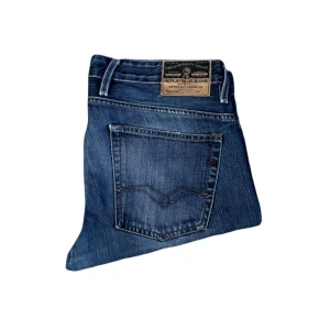 Replay jeans  - Snygga Replay jeans i klassisk blå tvätt med raka ben och normal passform. Jeansen har fem fickor, tydliga slitningar och Replay-logga på bakfickan. Tillverkade i slitstarkt bomullsjeansmaterial, perfekta för en avslappnad streetstil. Jag skickar ej bild när jag bär plaggen och jag vet ej vilken längd och vikt de passar då jag inte prövar kläderna jag säljer, så för storlek hänvisar jag till måtten och passform att man googlar på modellnamn etc 😃