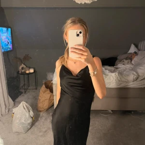 Svart satin klänning - En svart, klänning i satin med tunna axelband och snygg draperad urringning. Klänningen har en stilren och enkel design. dragkedja i ryggen och du kan ändra bandens längd 