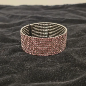 Glittrigt rosa armband - Brett armband i silverfärgad metall med massor av små rosa glittrande stenar över hela ytan. Perfekt statement piece för dig som vill sticka ut och addera extra bling till din outfit.