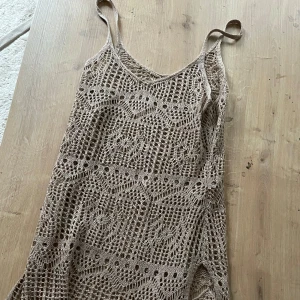 Beige virkad sommarklänning - Superfin beige virkad klänning med smala axelband och snyggt mönster. Perfekt för varma dagar eller som strandplagg. Klänningen har en luftig känsla och slits i nederkanten för extra vibe.