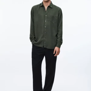 Daintree Lyocell Shirt from A Day's March - Stilren mörkgrön skjorta från A Day's March i mjuk bomull. Klassisk krage, bröstficka och knäppning framtill. Långärmad modell med normal passform, perfekt till svarta byxor eller jeans. Enkel och snygg design som funkar året runt.