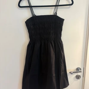 Svart kort klänning  - Supersöt svart kort klänning från H&M i storlek xs. Klänningen har smockad överdel, tunna dubbla axelband och en liten rosett baktill💕perfekt till sommaren!! Helt ny med prislapp, säljer en likadan fast i vit!