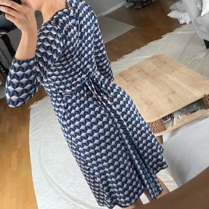 Mönstrad omlottklänning från Mango - Säljer en superfin omlottklänning från Mango med geometriskt mönster i blått, svart, ljusrosa. Klänningen har v-ringning, trekvartsärm och knyt i midjan. Perfekt för sommarkvällen!