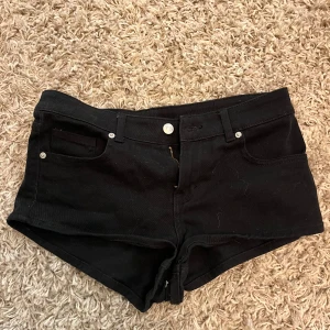 Svarta jeansshorts med låg midja - Snygga svarta jeansshorts med låg midja och klassisk femficksdesign. De är tighta och har bälteshällor, dragkedja och knapp framtill. 