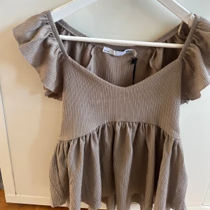 Beige volangblus - Supersöt beige blus med volangärmar och v-ringning. Blusen har en lös passform och är tillverkad i ett mjukt, strukturerat bomullstyg. Perfekt för dig som gillar en romantisk och avslappnad stil. Helt oanvänd med prislapp kvar💕