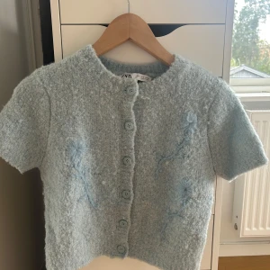 Ljusblå stickad kofta från Zara - Superfin ljusblå stickad kofta från Zara med korta ärmar och rund hals. Koftan har stora knappar framtill och broderade blommor i samma färg på både fram- och baksidan. Nästan aldrig använd och går inte att köpa längre. Storlek S men passar även XS. 💕
