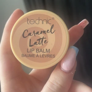 Technic Caramel Latte Lip Balm - Säljer ett veganskt läppbalsam från Technic i smaken Caramel Latte. Kommer i en rund burk på 14g med beige och karamellfärgad design. Perfekt för att hålla läpparna mjuka och återfuktade med en söt doft av karamell.