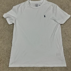 Vit t-shirt från Ralph Lauren - Vit t-shirt från Ralph Lauren med klassisk blå broderad logga på bröstet. Modellen är slim fit och har rund halsringning samt korta ärmar. Tillverkad i mjuk bomull som känns skön mot huden.                                              Oanvänd men utan prislapp  Priset går att diskuteras! Fraktas inom 1-2 dagar! 🚛
